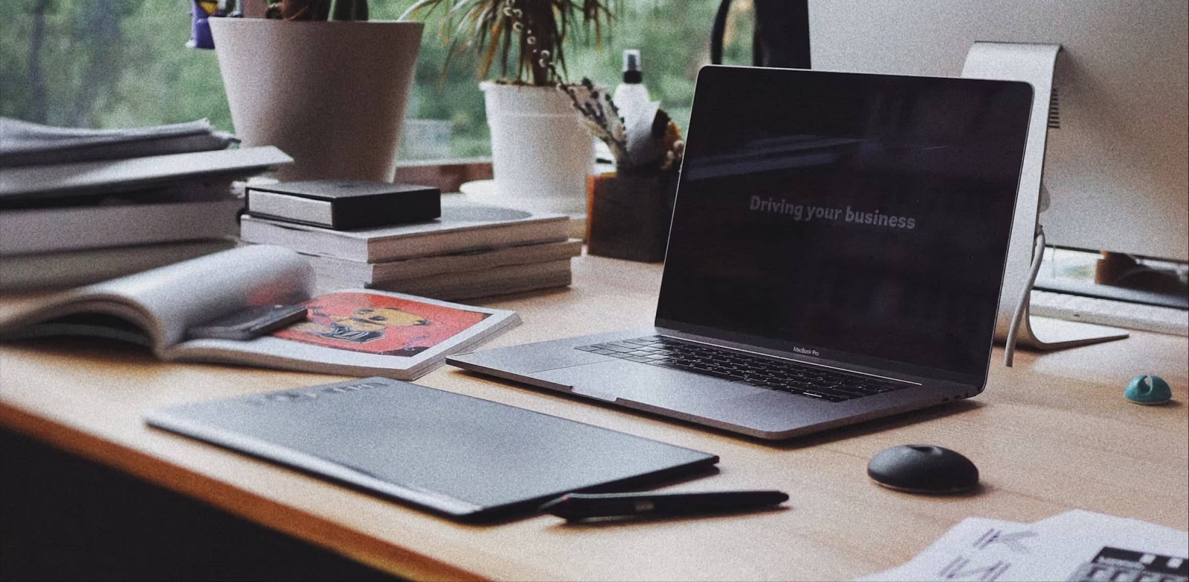 A table set up by the window with a laptop, mouse and other stationeries on the table